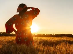 Woman in a field of crops looking into the distance as the sun sets